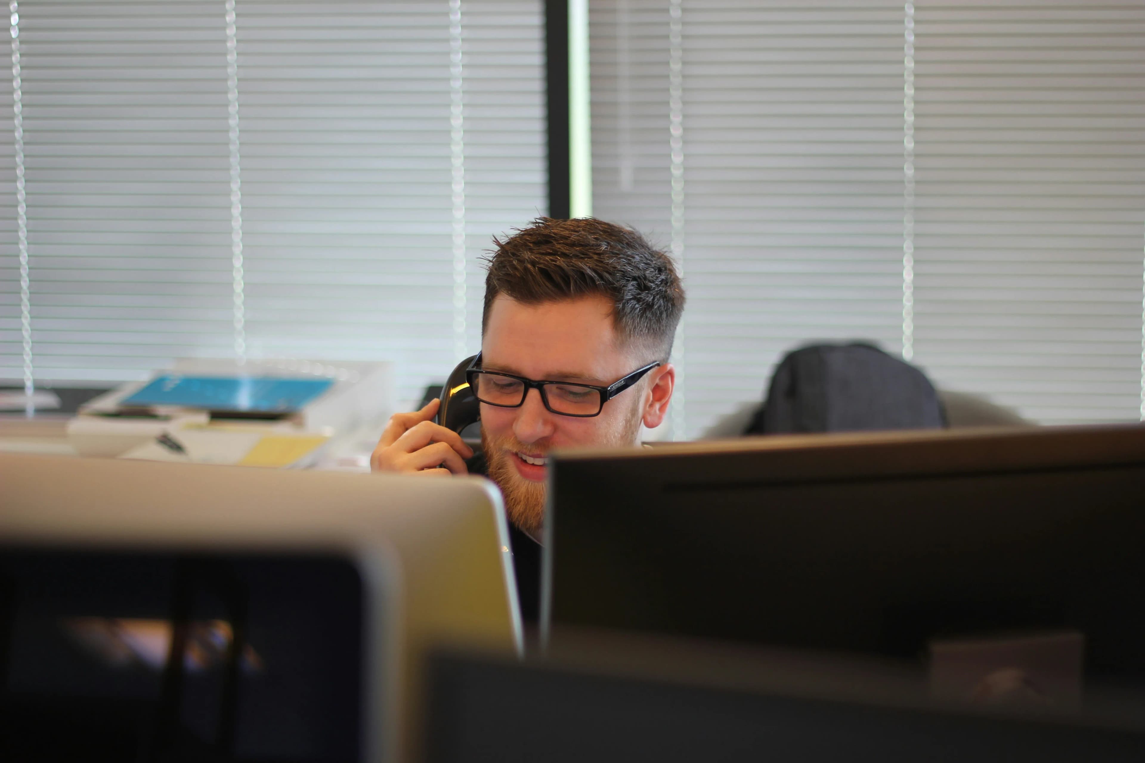 A man is sitting in front of computers and talking to a customer.